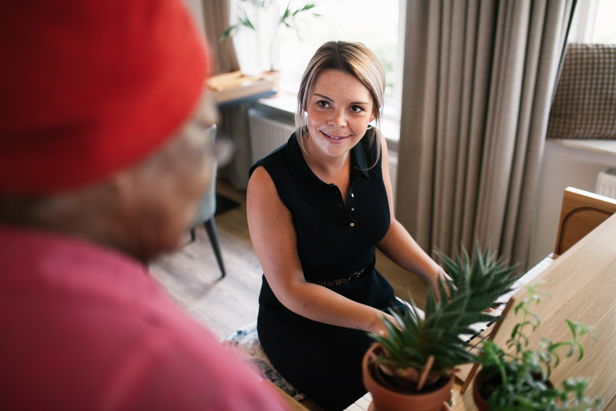 Medewerker van Maanderzand in gesprek met oudere bewoner tijdens persoonlijke zorg en begeleiding in het verpleeghuis.